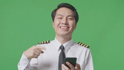 Man Pilot Smiling And Pointing To Smartphone In His Hand Standing Green Screen Stock Footage 244397246