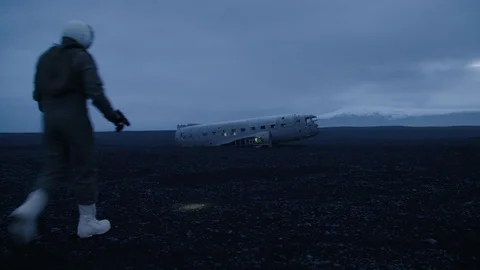 Man in pilot suit get to a wrecked plane on Iceland beach Stock Footage 104238741
