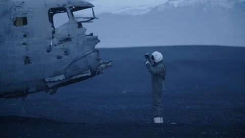 Man in pilot suit looking at a wrecked plane on an Iceland beach Stock Footage 104238978