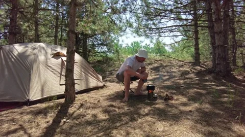 Man in Pine Forest Boiling Kettle on Wood Fire During Summer Stock Footage 291894986