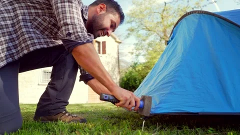 Man pitching camping tent hammering stake Vidéo 333386681