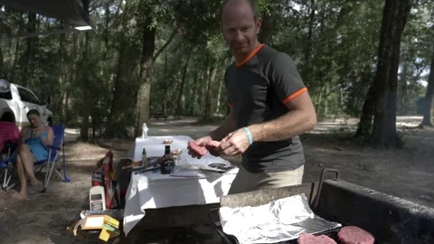Man Places Burgers on Grill in Campground Stock Footage