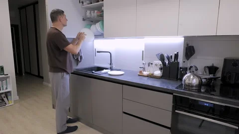 Man placing clean dishes into kitchen cabinet after household washing Stock Footage 336307525