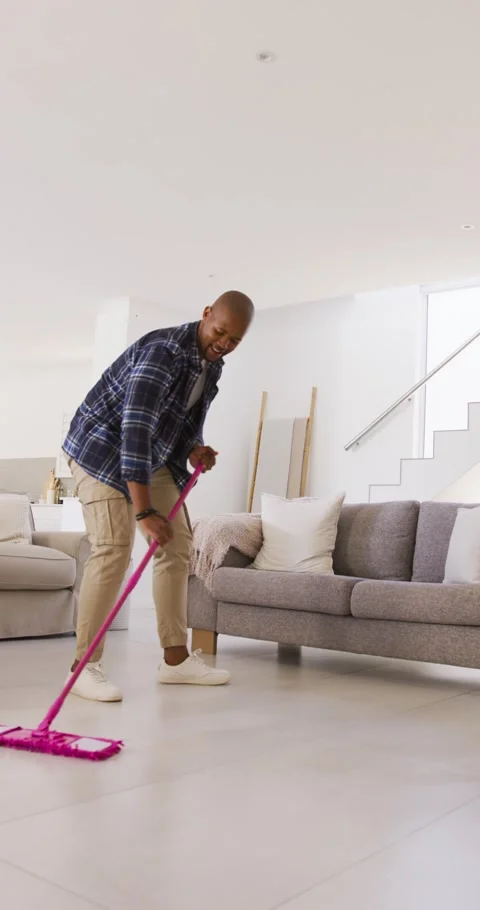 Man placing pink mop head on tile and mopping toward sofas, narrowing strokes Stock Footage 345322699