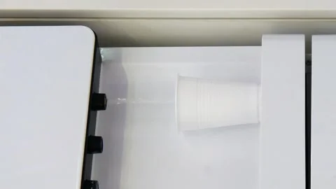 A man placing a plastic cup under a cooler tap to fill it with water. Vertical Stock Footage 328441244
