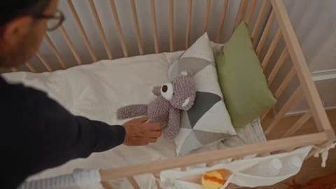 Man placing teddy bear in crib within cozy bedroom setting, highlighting nu.. Stock Footage 311022150