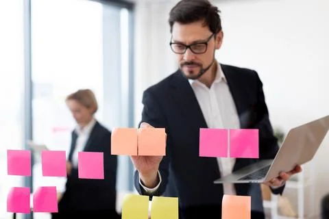 Man planning on sticky notes, holding a laptop, office in background Fotos de archivo