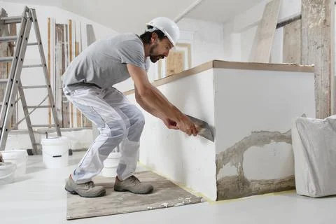 Man plasterer construction worker at work, takes plaster from bucket and puts Stock Photos