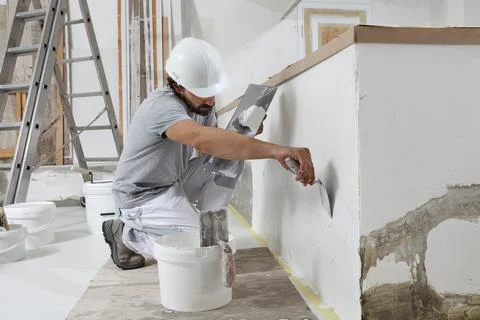 Man plasterer construction worker at work, takes plaster from bucket and puts Stock Photos