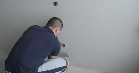 Man plasterer with trowel aligns final layer of plaster on wall, removes stains Stock Footage 129837157