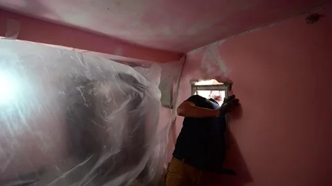 Man plastering the wall around a small window during renovation Stockbeeldmateriaal 347640500
