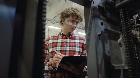 Man in plastic glasses writing with pen in tablet at work, front of manufactury Stock Footage 110796349