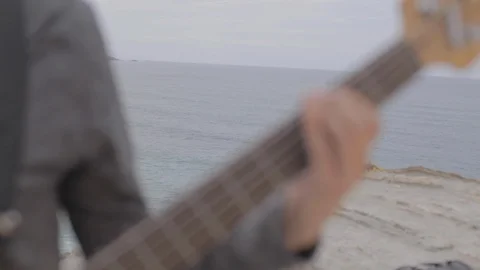 Man playing 5-string electric bass on top of a cliff, outdoors, by the sea in Stock Footage 110914672