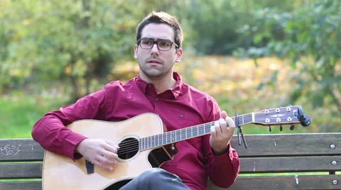Man playing acoustic guitar and singing in park Stock Footage 59556509