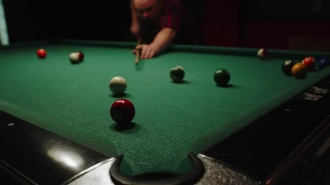 Man is playing billiards, hitting white ball with cue aiming at red one and Stock Footage 172312891