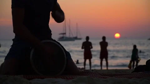 A man is playing on a djembe drum on the beach at sunset. Stock Footage 83405474