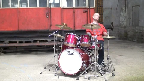 Man playing the drumset in red outfit - Old train repair factory, Stock-Footage 104472483