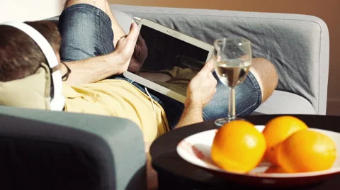 Man playing game on tablet and wearing headphones while lying on the sofa Stock-Footage 63206523