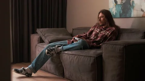 A man playing games on a console at home sitting on the couch. Video stock 238479669