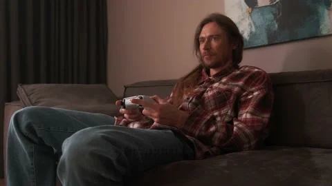 A man playing games on a console at home sitting on the couch. Stock Footage 238479939