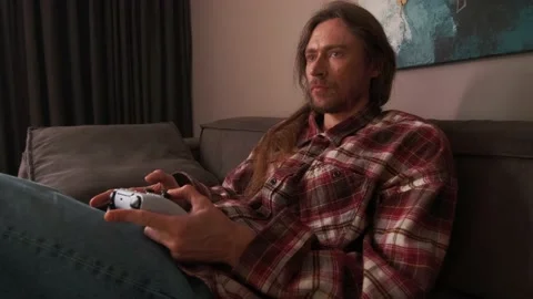 A man playing games on a console at home sitting on the couch. Stock Footage 238480049