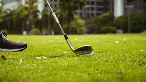 Man playing golf on golf course in city, swinging and hitting golf ball in slow Stock Footage 177991849