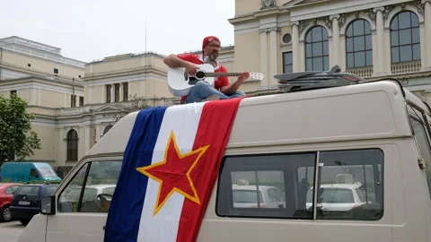 Man playing guitar and singing Bella ciao above ex-Yugoslavian flag Stock Footage 140457375