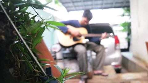 Man playing guitar in a backyard in background blurry Stock Footage 276409566