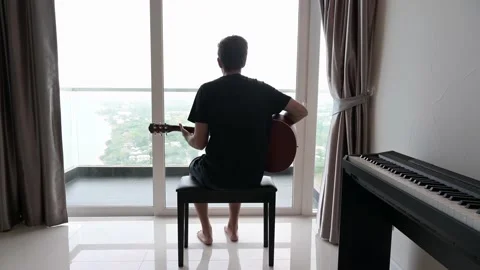 Man playing guitar looking out window Vidéo 164728959