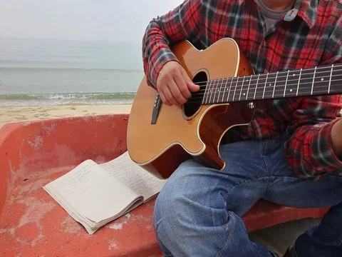 Man playing guitar sitting in a boat on the beach Video stock 82586666