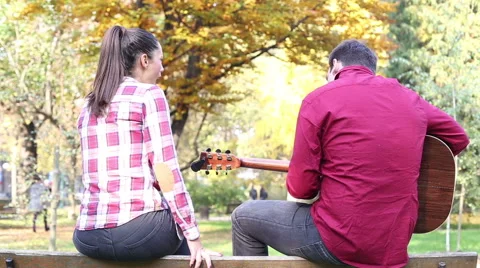 Man playing guitar while woman singing in park Stock Footage 59556921