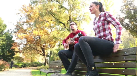 Man playing guitar while woman dancing to the rhythm, sitting next to him on Stock Footage 59557056
