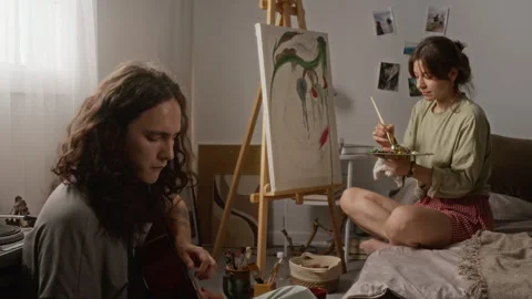 Man Playing Guitar While Woman Painting on Canvas at Home Stock Footage 345233907