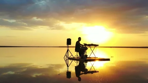 A man is playing hang drum with stunning colorful sunset in the background, 4k Stock Footage 143543094