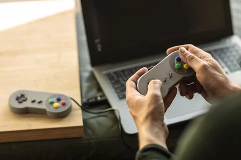 A man playing on his laptop computer with a classic old school gaming console 스톡 사진