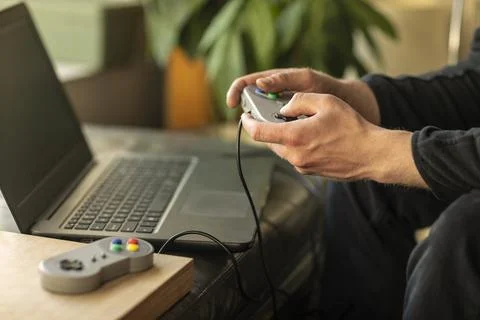 A man playing on his laptop computer with a old school classic gaming console Stock-Fotos