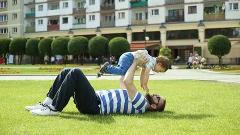 Man playing with his son on the grass in the park and enjoying this Stock Footage 76981158
