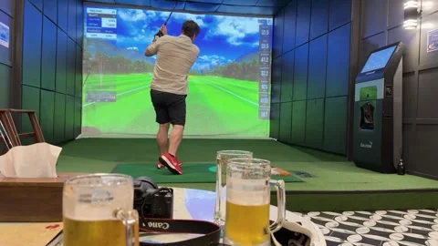 Man Playing Indoor Golf Simulator With Drinks Nearby Stock Footage 323981843