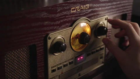 A man playing with the knobs on a Craig vinyl record player at dusk. 動画素材 148066126