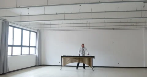 Man playing marimba  wearing white outfit in a blank empty room with windows. Stock Footage
