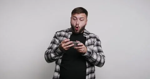 Man playing mobile game while smiling in a plain room with white wall durin.. Vídeos de archivo 326798545