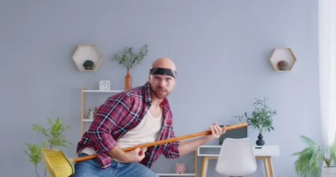 Man playing mop as rock guitar, having fun, pretending rock band famous star Stock Footage 265599010