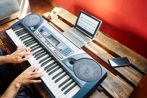 A man playing the piano at home while using a tablet to read the scores and t Stock Photos