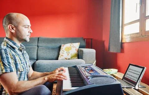 Man playing piano while taking online lessons. Stock Photos