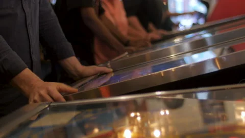 Man playing at a pinball table in a busy arcade Video stock 130989880