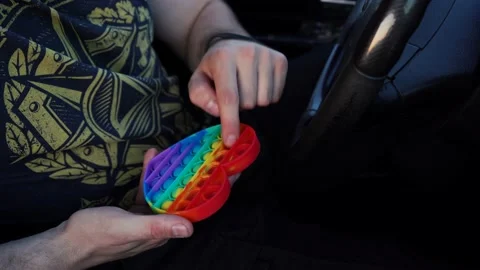 Man playing rainbow pop it while sitting in the car Stock Footage 168874301