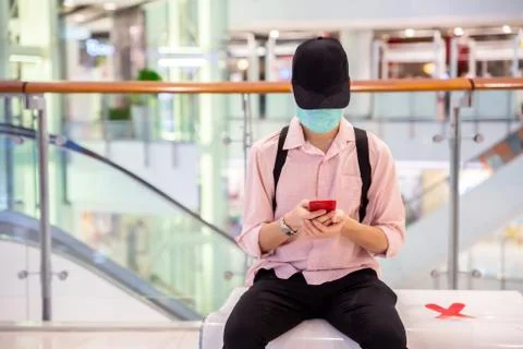 A man is playing a smartphone while sitting on a public shopping mall bench w Stock Photos