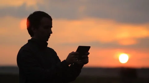 A man playing on a tablet in the game. Beautiful sunset on the background Stock Footage 64601227