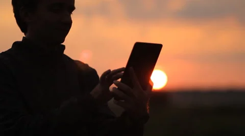 A man playing on a tablet in the game. Beautiful sunset on the background Stock Footage 64601388