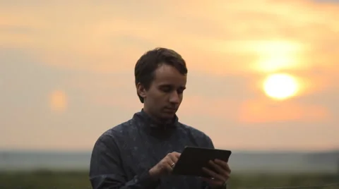 A man playing on a tablet in the game. Beautiful sunset on the background Stock Footage 64601523